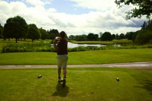 beautiful golf day golfer during back swing from behind on the tee shot front of lake and green in Par three